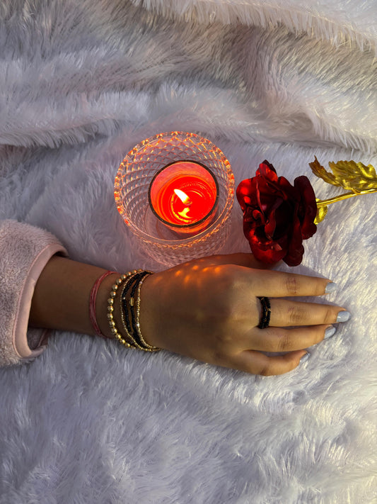 Hand with bracelets holding a red rose next to a lit candle on a fluffy white surface