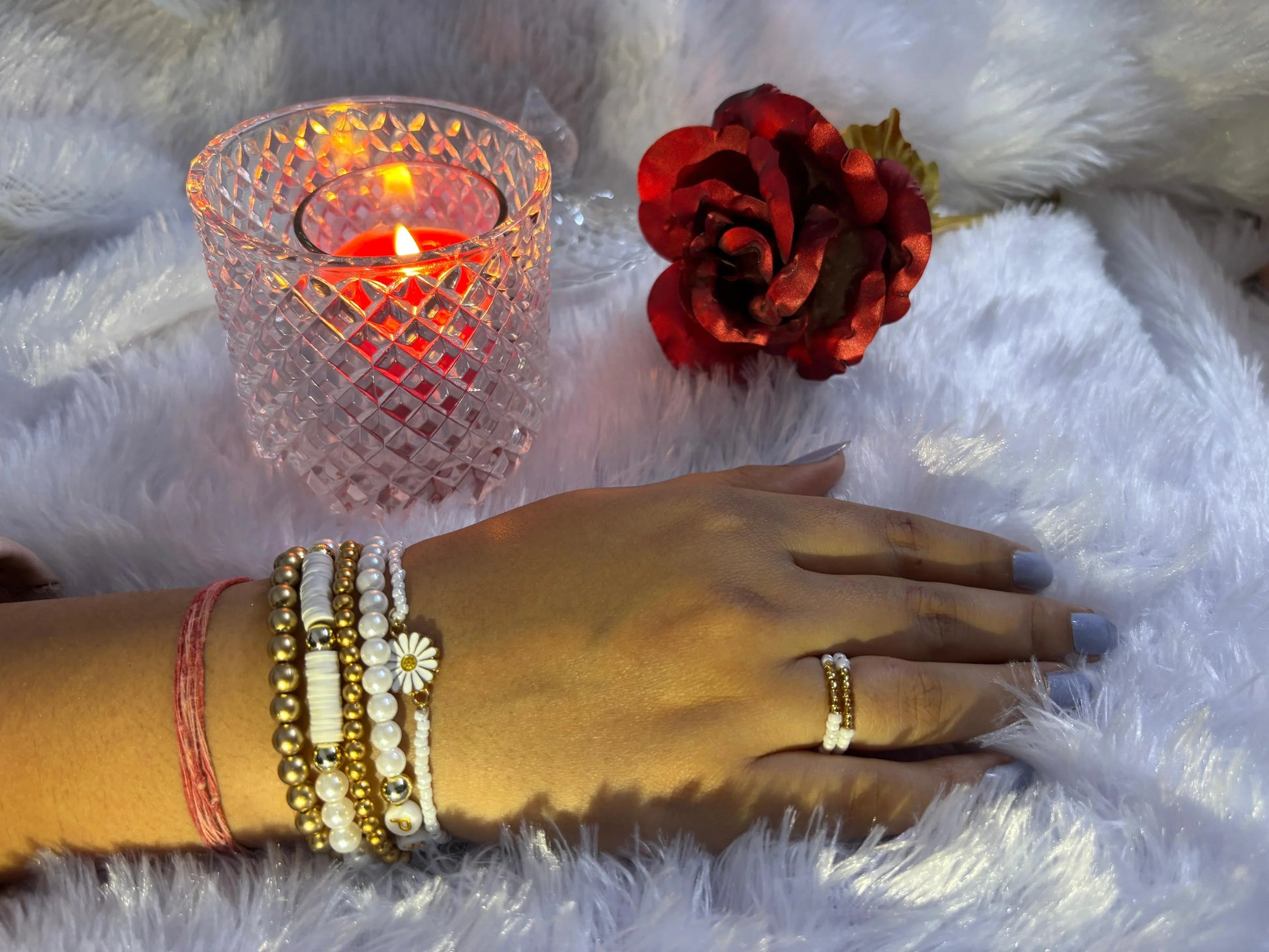 Hand with bracelets near a lit candle and red flower on white fur