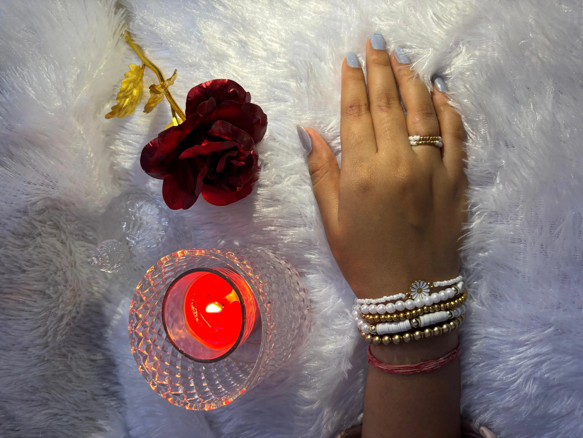 Hand with bracelets near a red flower and candle on white fur