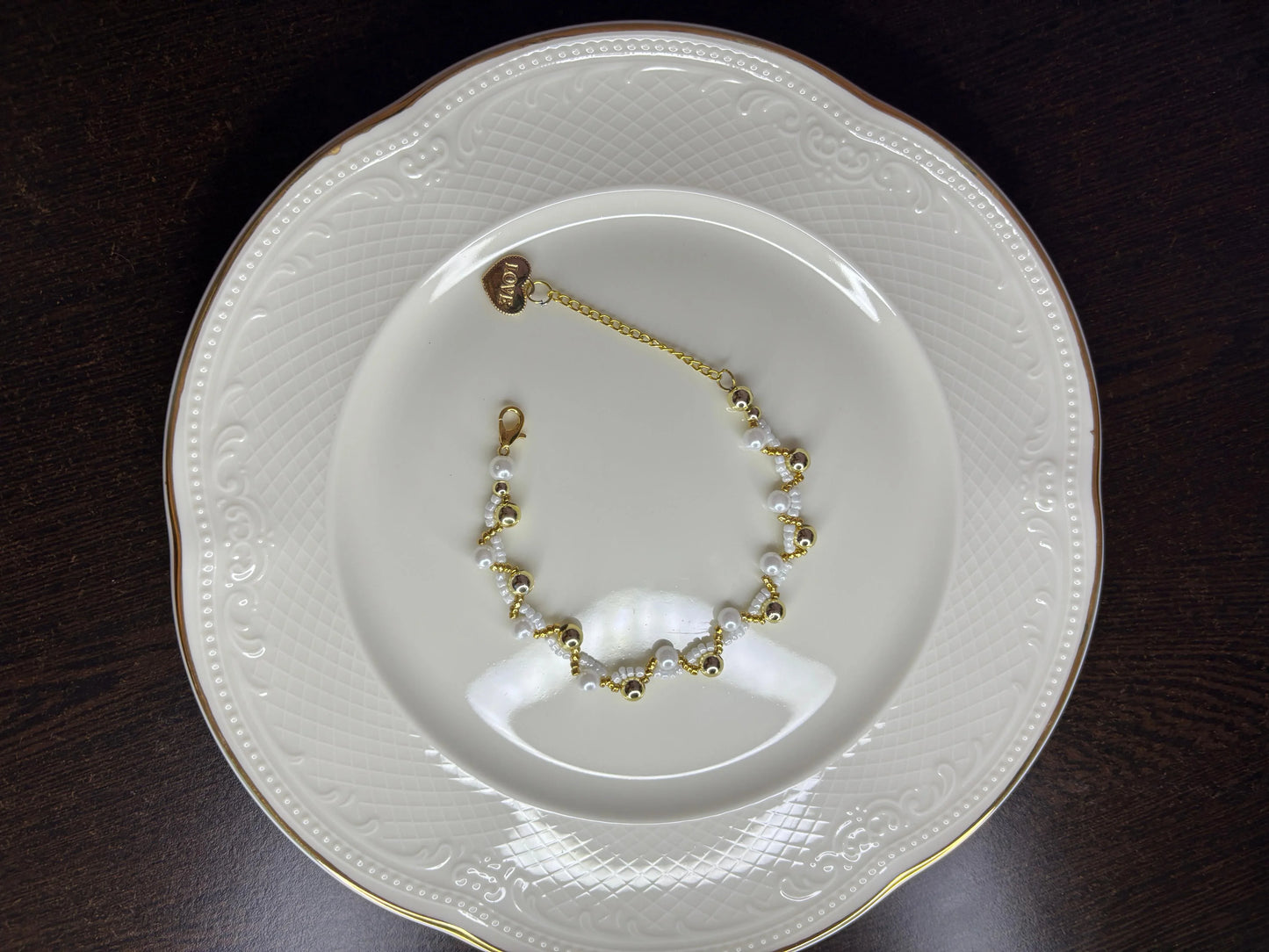 Gold and white bracelet on a decorative white plate with gold rim on a dark surface