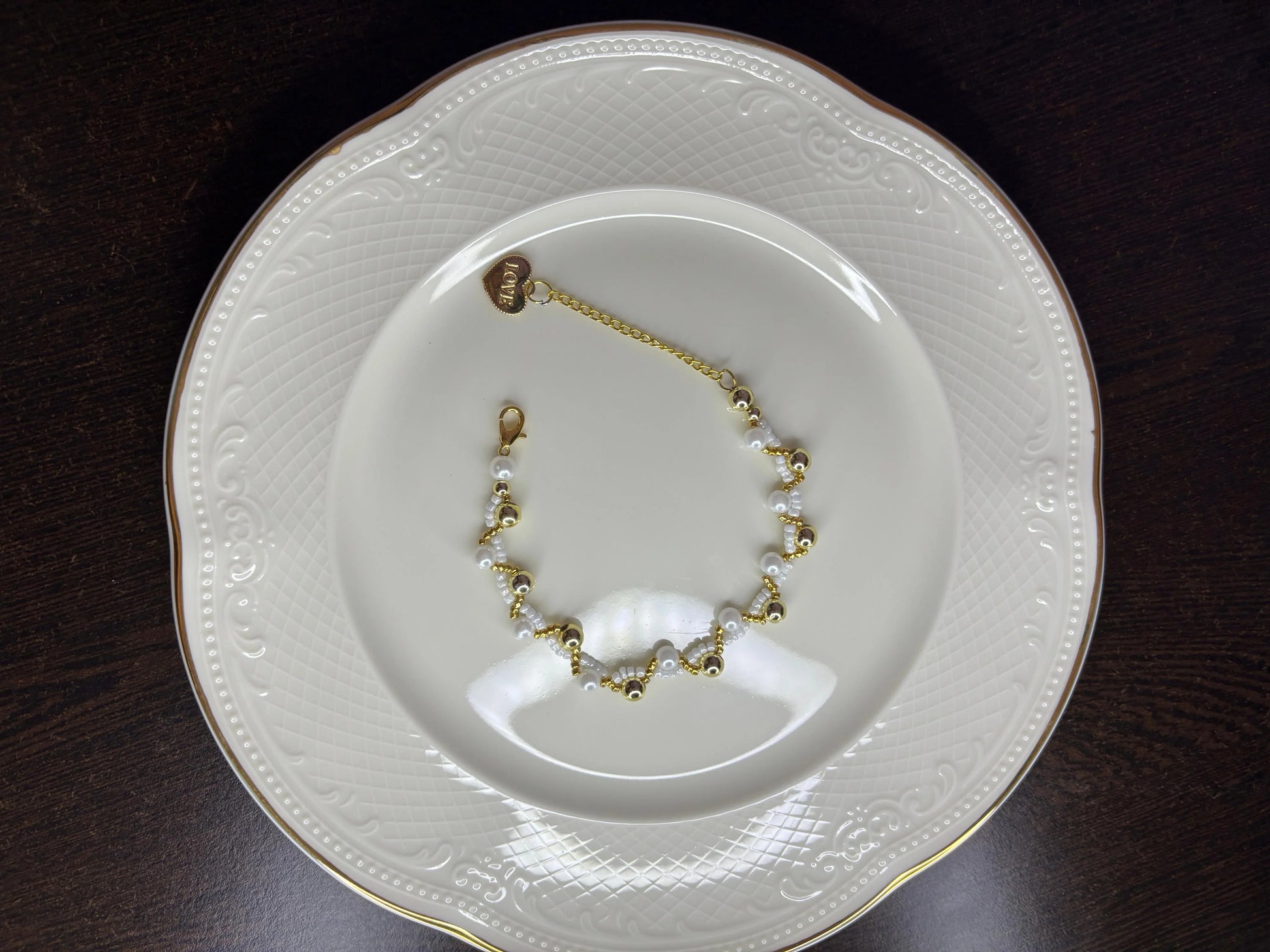 Gold and white bracelet on a decorative white plate with gold rim on a dark surface
